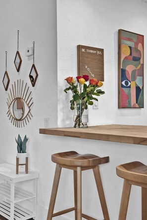 A modern interior with a wooden bar, bar stools, a mirror, a vase with flowers, and wall art. - Chic Condo w/ Patio, Near Fort Lauderdale Hotspots (Fort Lauderdale)