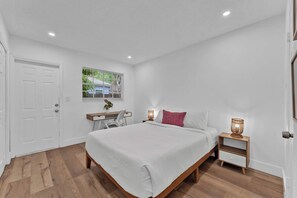 A bedroom with a bed, bedside tables, a desk, and a window with blinds.