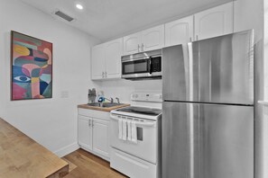 A compact kitchen with white cabinetry, a stainless steel refrigerator, a microwave, an oven, and a sink.