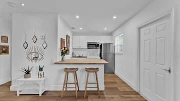 A modern kitchen with white cabinetry, a stainless steel refrigerator, and a wooden island with bar stools.