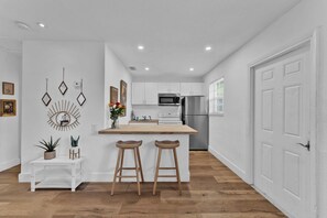 A modern kitchen with white cabinetry, a stainless steel refrigerator, and a wooden island with bar stools.