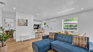 A modern living room with a blue sectional sofa, a dining area with a yellow table, and a kitchen in the background. - Flamingo Escape: Bright 2BR Near Riverside Beach (Fort Lauderdale)