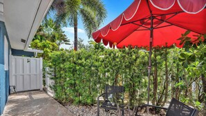 A patio with a red umbrella, two metal chairs, a white fence, and lush greenery. - Flamingo Escape: Bright 2BR Near Riverside Beach (Fort Lauderdale)