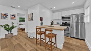A modern kitchen with white cabinetry, a stainless steel refrigerator, and a wooden island with two bar stools. - Flamingo Escape: Bright 2BR Near Riverside Beach (Fort Lauderdale)