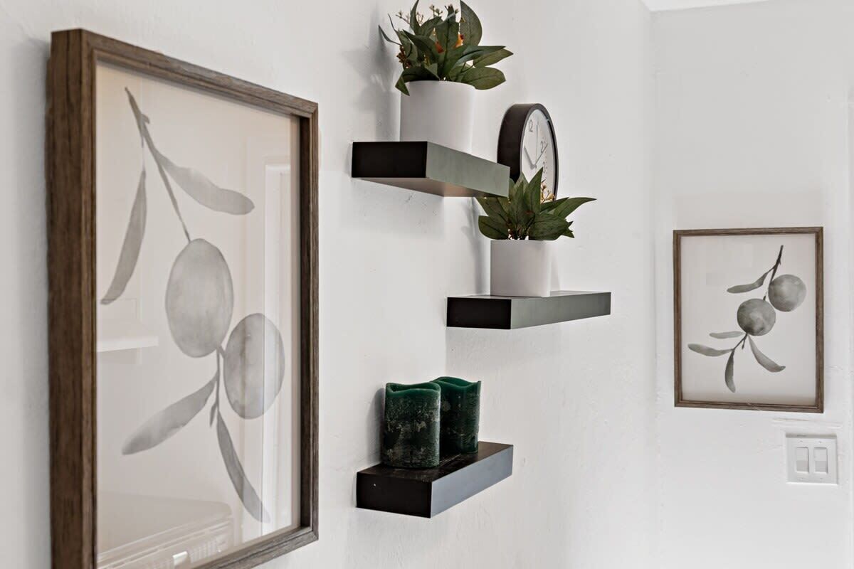 A wall with a framed artwork, a clock, and two shelves with decorative items.