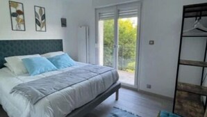 A bedroom with a bed, a bench, a wardrobe, and a sliding glass door leading to a balcony. - La Parenthèse Gîte 3 Étoiles à la Campagne (Fougerolles-Saint-Valbert)