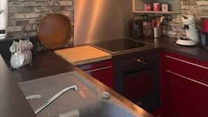 A modern kitchen with a stone wall backsplash, stainless steel appliances, and red cabinetry. - La Parenthèse Gîte 3 Étoiles à la Campagne (Fougerolles-Saint-Valbert)
