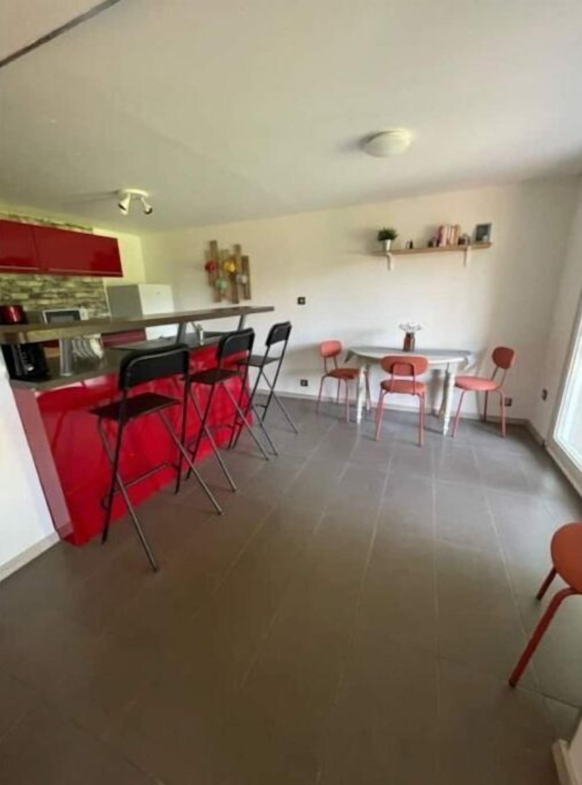 Une cuisine de taille réduite avec des meubles de rangement rouges et un coin repas comprenant une table ronde et des chaises.