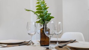 Une table à manger dressée avec des assiettes, des couverts et des verres à vin, et une plante décorative placée au centre.