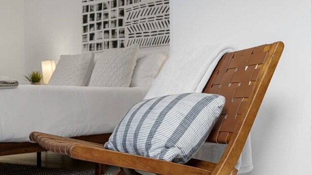 Une chaise en bois avec un coussin à carreaux, dans une pièce moderne avec un lit blanc et un mur à motifs.