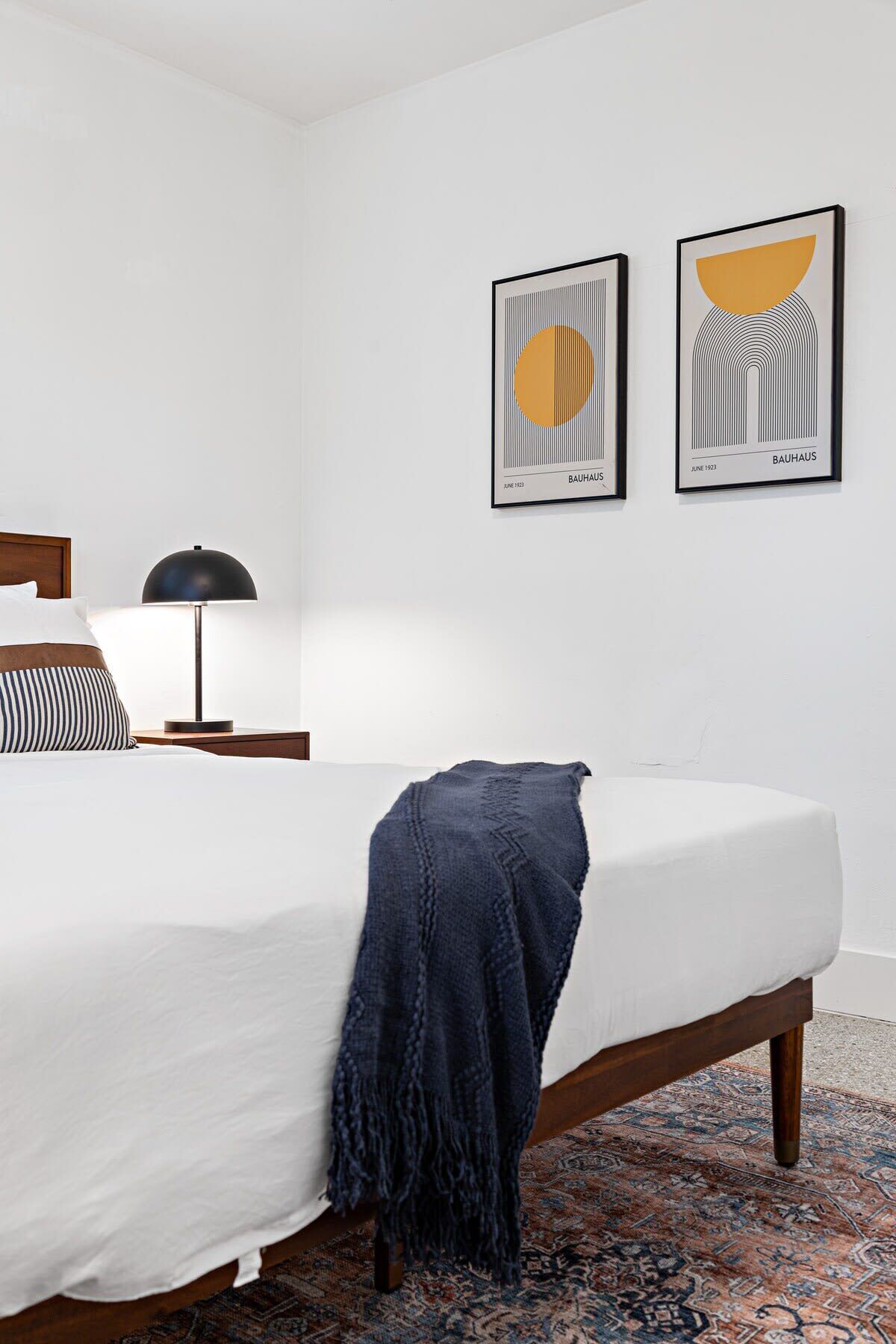 A modern bedroom with a large bed, a bedside lamp, a throw blanket, and two framed artworks on the wall.