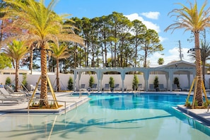 A swimming pool with lounge chairs, palm trees, and a covered seating area.