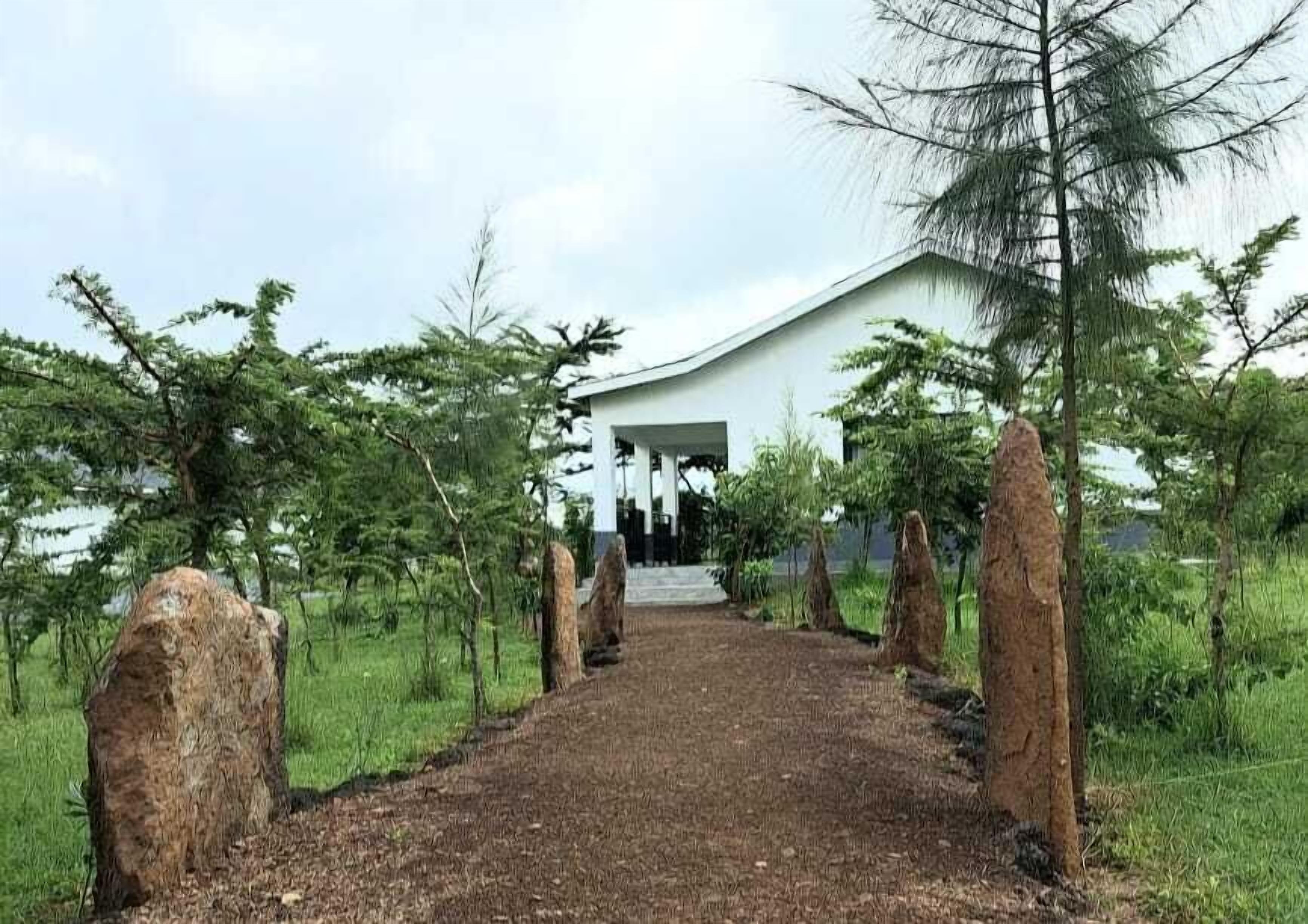 A white building with a covered entrance and a dirt path leading to it, surrounded by trees and grass.