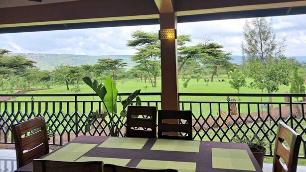 A covered outdoor seating area with a table and chairs, overlooking a lush landscape with trees and a distant view of hills. - Iretet Mara Lodge (Maasai Mara)