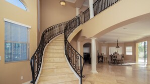 A spacious interior with a curved staircase, large windows, and a dining area. - Spacious Golf Course Retreat on Hogan (Lake Havasu City)