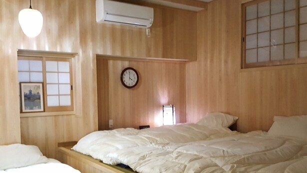 Une pièce aux murs lambrissés, un lit avec une literie blanche, une horloge murale et un appareil de climatisation.