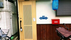 Une entrée d’immeuble avec une porte en bois, une lanterne bleue, un panneau indicateur et une boîte aux lettres rouge.