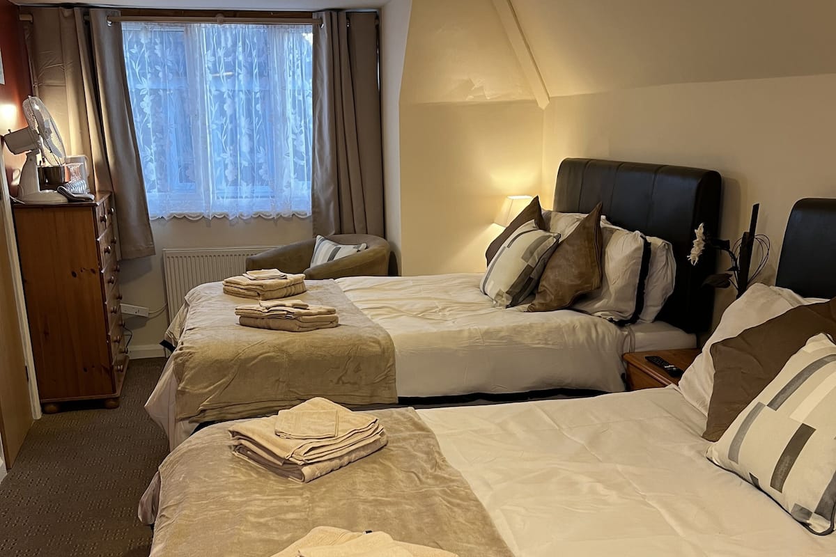 A hotel room with two beds, a desk with a lamp, a dresser, and a window with curtains.