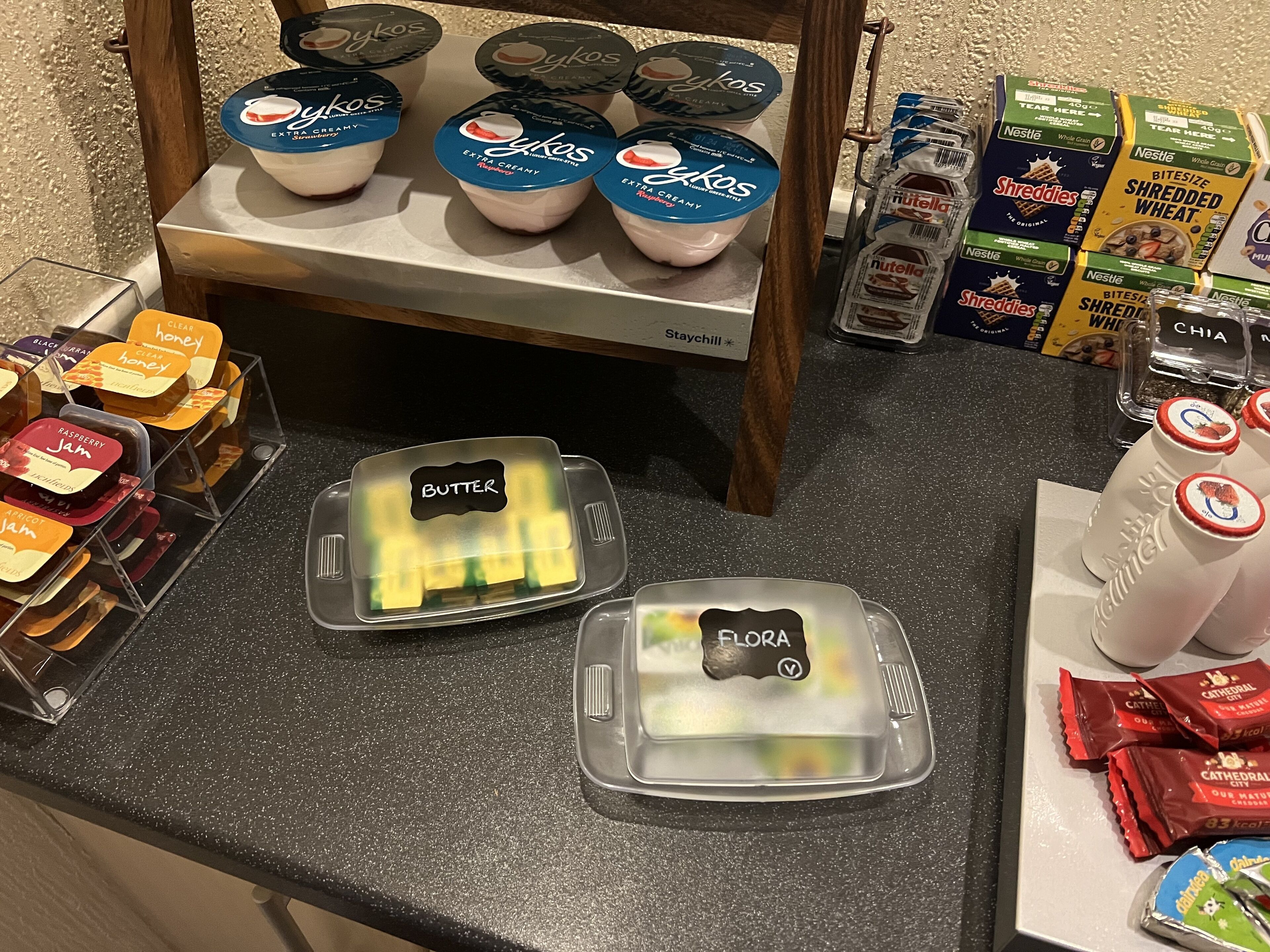 Een ontbijtbuffet met diverse soorten eten, zoals yoghurt, ontbijtgranen, boter, jam en gebak.
