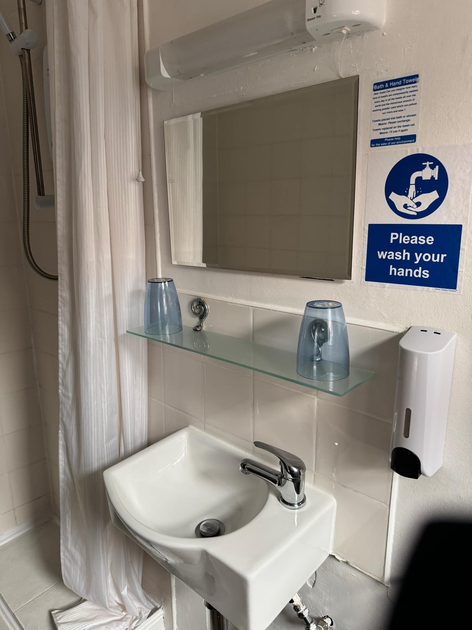 A bathroom with a white sink, a glass shelf with toiletries, a hand soap dispenser, and a mirror.