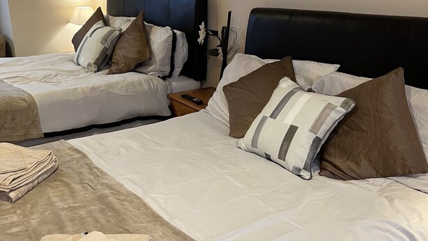 A hotel room with two beds, each with white bedding and brown pillows. There are folded towels on the bed and a remote control on a nightstand. - The Singlecote Hotel (Skegness)