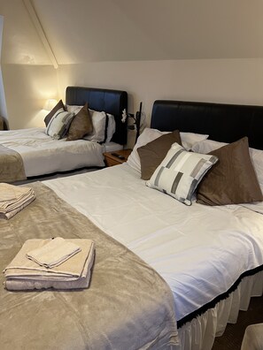 A hotel room with two beds, each with white bedding and brown pillows. There are folded towels on the bed and a remote control on a nightstand. - The Singlecote Hotel (Skegness)