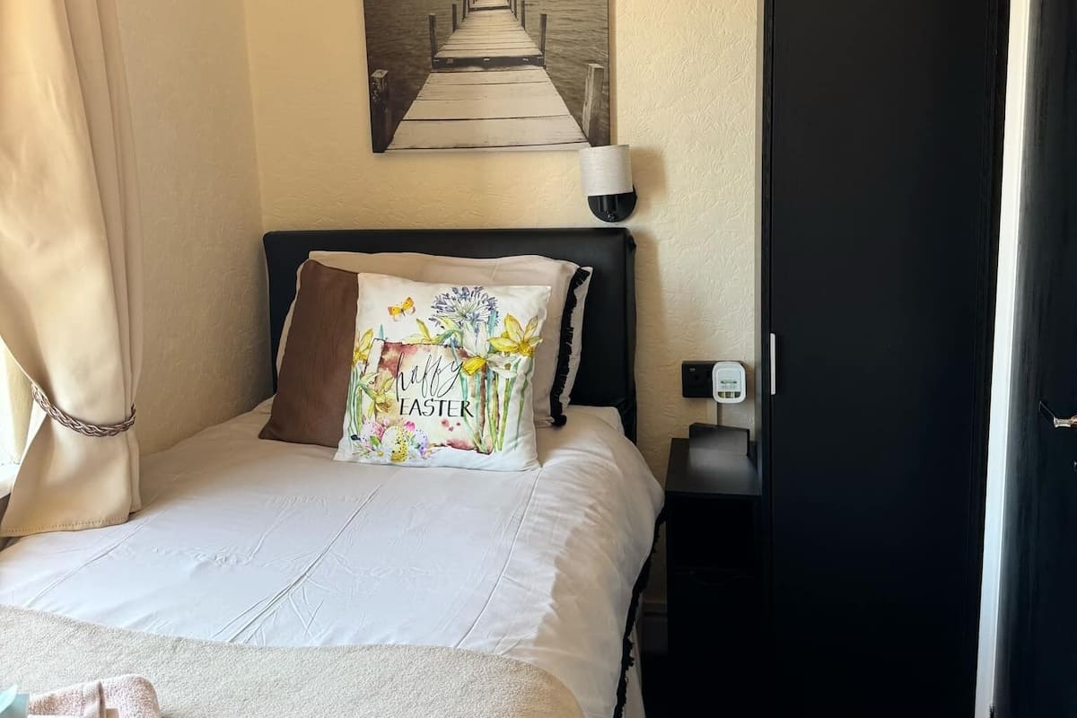 A hotel room with a bed, a wall-mounted fan, a door, and a painting of a pier.