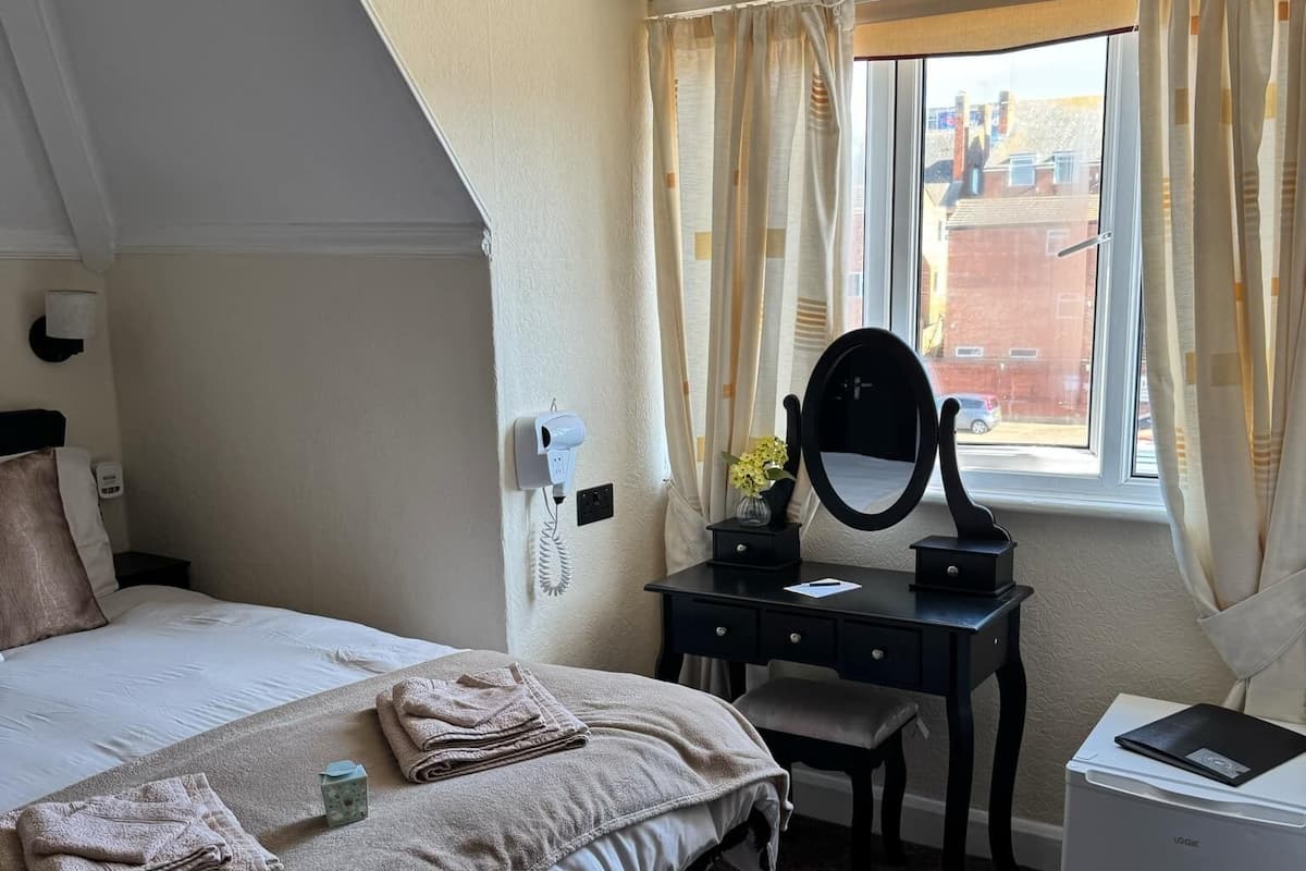 A bedroom with a bed, a desk with a mirror, and a window with curtains.
