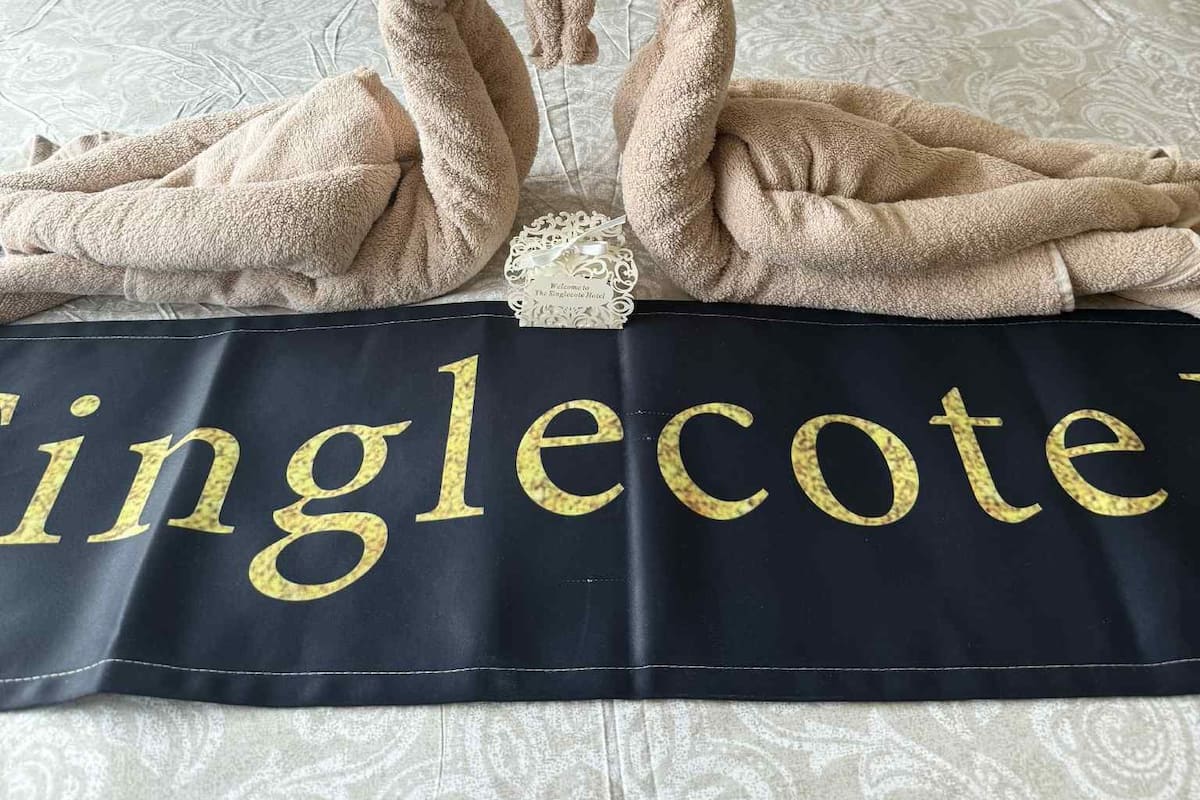 A bed with a towel arrangement in the shape of swans, a pillow with 'Summer' text, and a bedspread with 'The Singletcot Hotel' text.