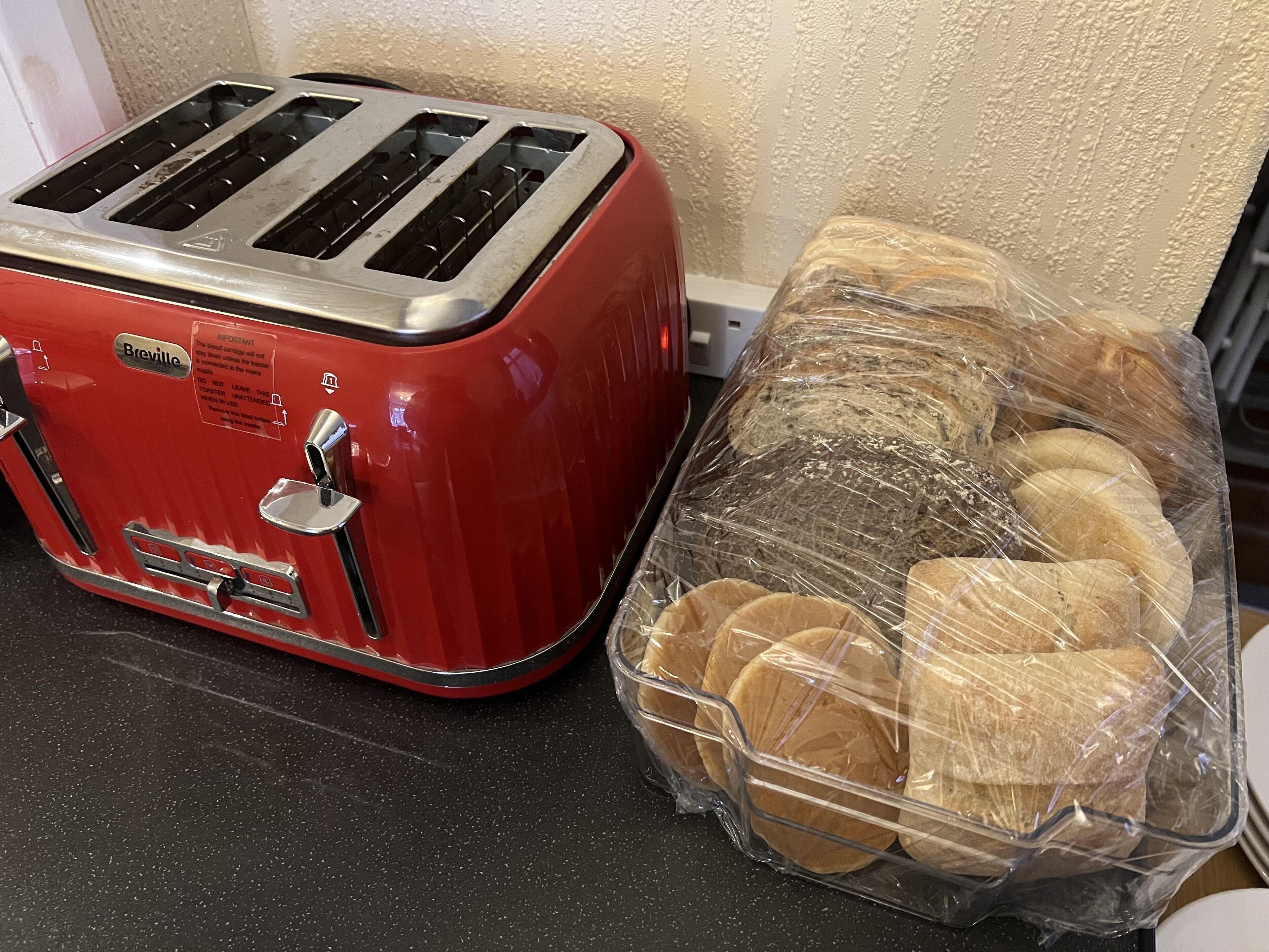 A red Breville toaster and a plastic container with bread rolls on a kitchen counter.