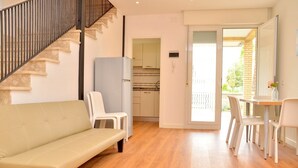 A modern living room with a sofa, chairs, a staircase, a kitchen, and a sliding glass door leading to an outdoor area. - Lovely Peaceful Villa Near the Beach-beahost (San Michele al Tagliamento)