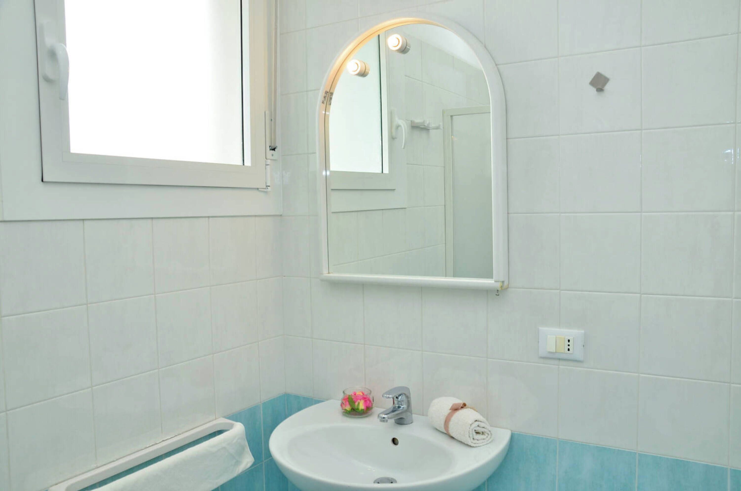 Een badkamer met een wit wastafelmeubel, een spiegel en een raam.