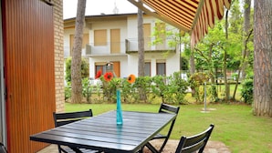 A patio with a table and chairs, a vase with flowers, and a building with balconies in the background. - Lovely Peaceful Villa Near the Beach-beahost (San Michele al Tagliamento)