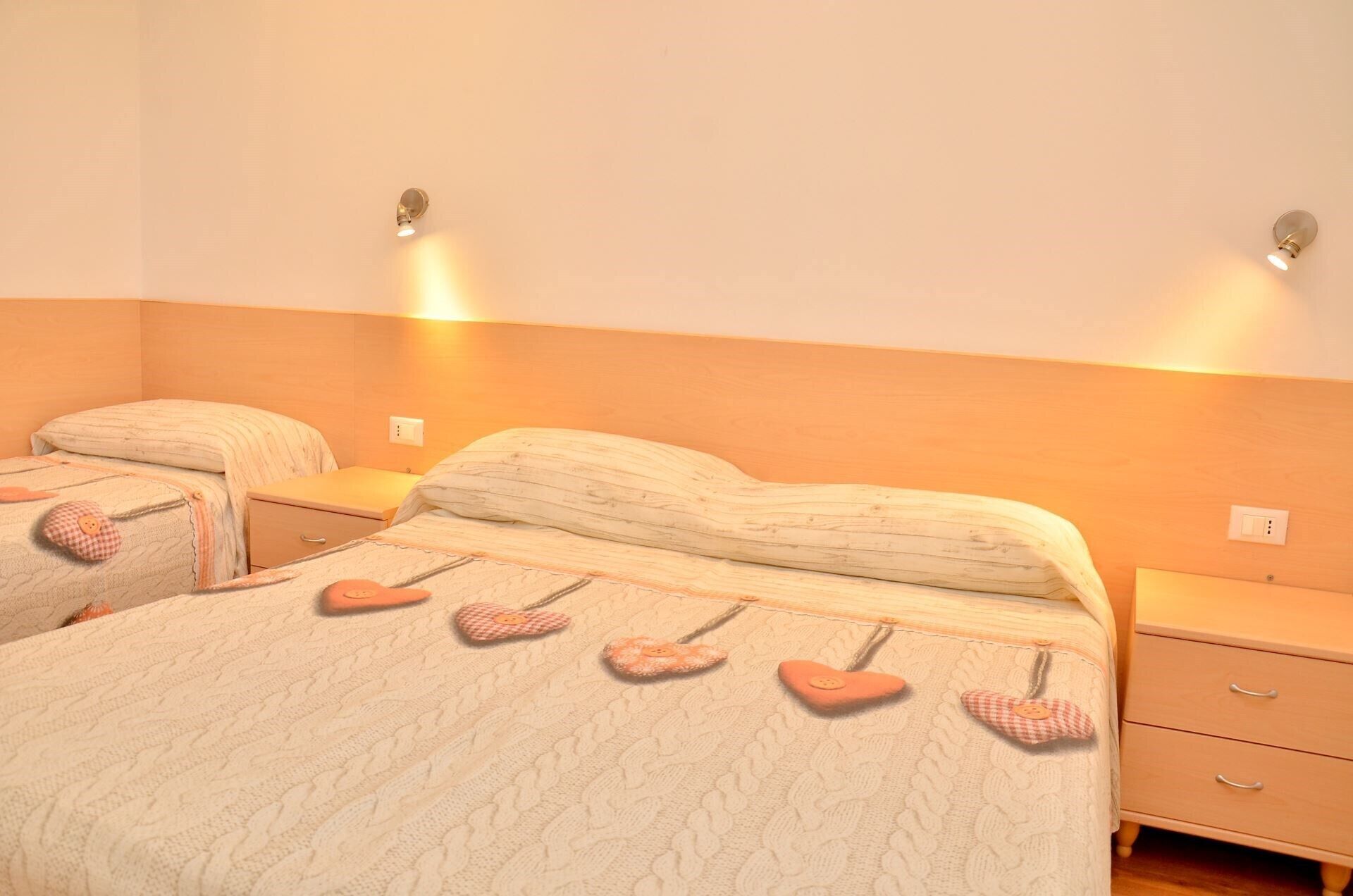 A bedroom with two beds, each with a heart-shaped pillow and a bedside table.