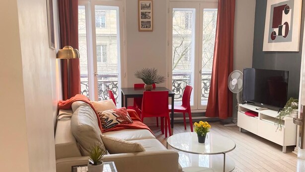 Ein modernes Wohnzimmer mit einer Couch, einem Couchtisch, einer TV-Kommode und einem Balkon mit roten Vorhängen.