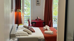 Ein Hotelzimmer mit Bett, Schreibtisch, Stuhl, Tisch mit Blumenvase und einem Vorhangfenster.