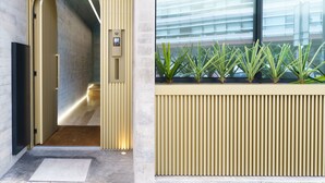 Un intérieur moderne avec un couloir menant à un ascenseur, un comptoir d’accueil agrémenté de plantes et une grande fenêtre équipée de stores.
