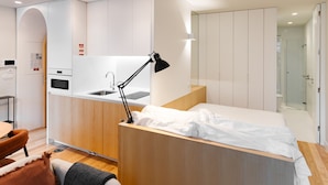 Une chambre d’hôtel de taille réduite, équipée d’une kitchenette, d’un lit, d’un bureau et d’une salle de bain.