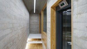 Un couloir étroit doté d’un plancher en bois, d’un mur en béton et d’une porte munie d’un écran numérique.