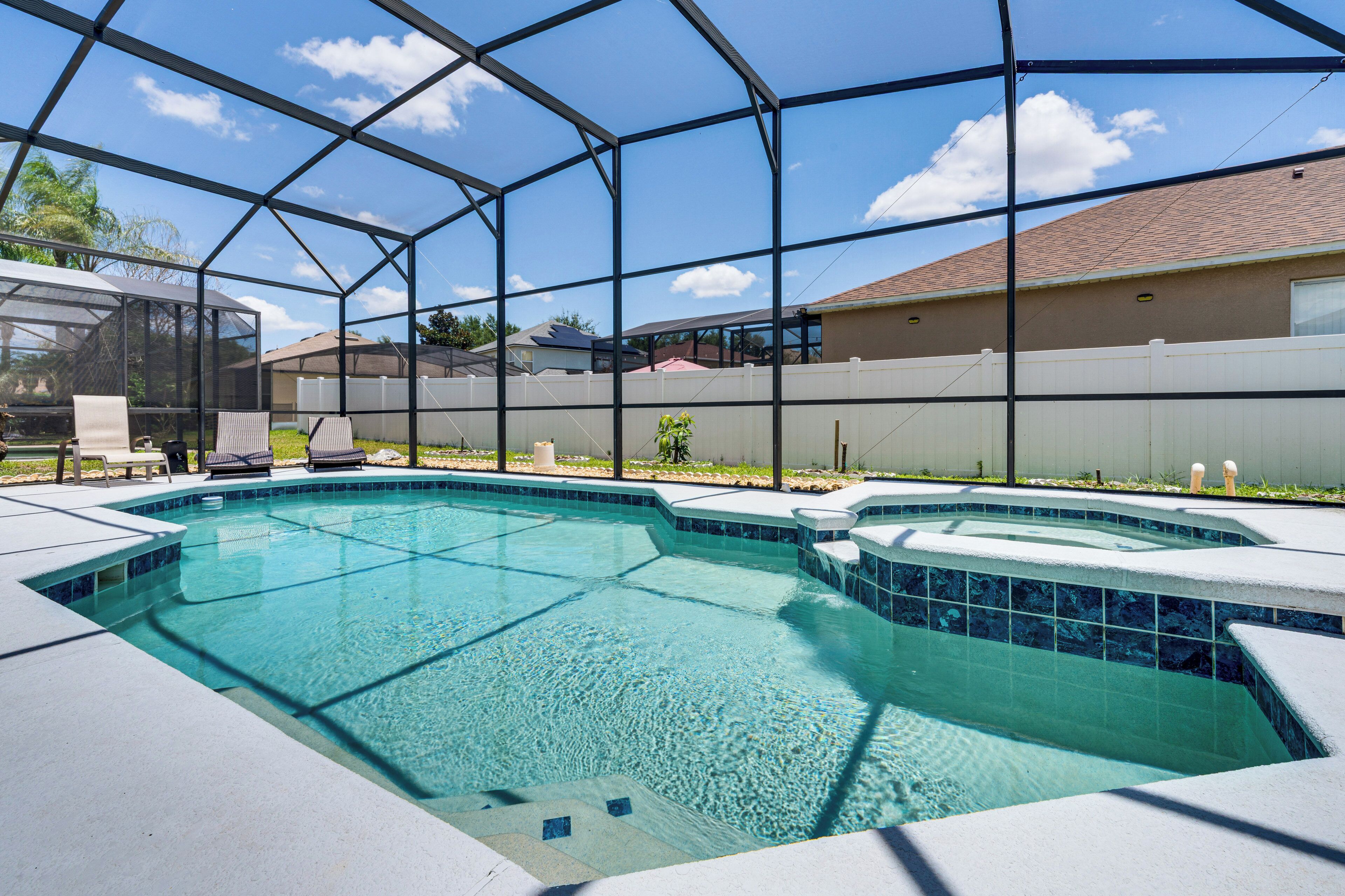 A swimming pool with a glass enclosure, surrounded by a white fence, and a house in the background.