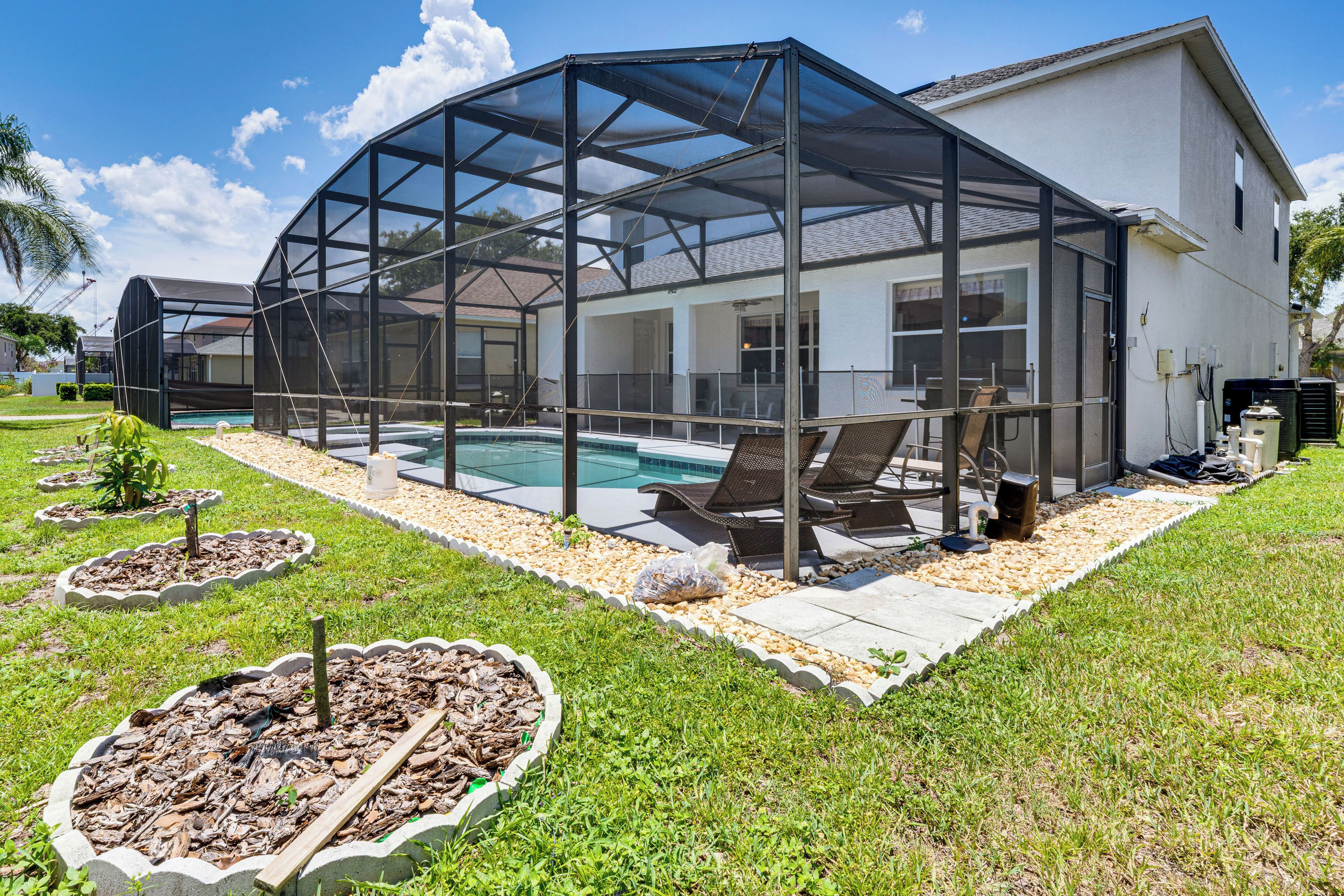Una casa con terraza cubierta, piscina y césped con jardineras.