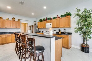 A modern kitchen with wooden cabinets, a central island, bar stools, and a potted plant. - Spacious Kissimmee Villa w/ Private Pool & Hot Tub (Kissimmee)