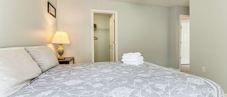 Un dormitorio con cama, mesita de noche con lámpara, ventilador de techo y puerta que da a otra habitación.