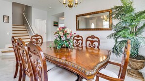Une salle à manger avec une table en bois, des chaises, un lustre, un miroir et une plante en pot.