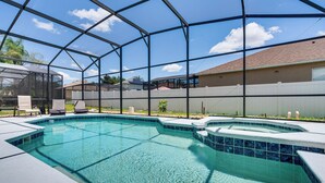 Une piscine entourée d’une enceinte en verre, elle-même bordée d’une clôture blanche, avec une maison en arrière-plan.