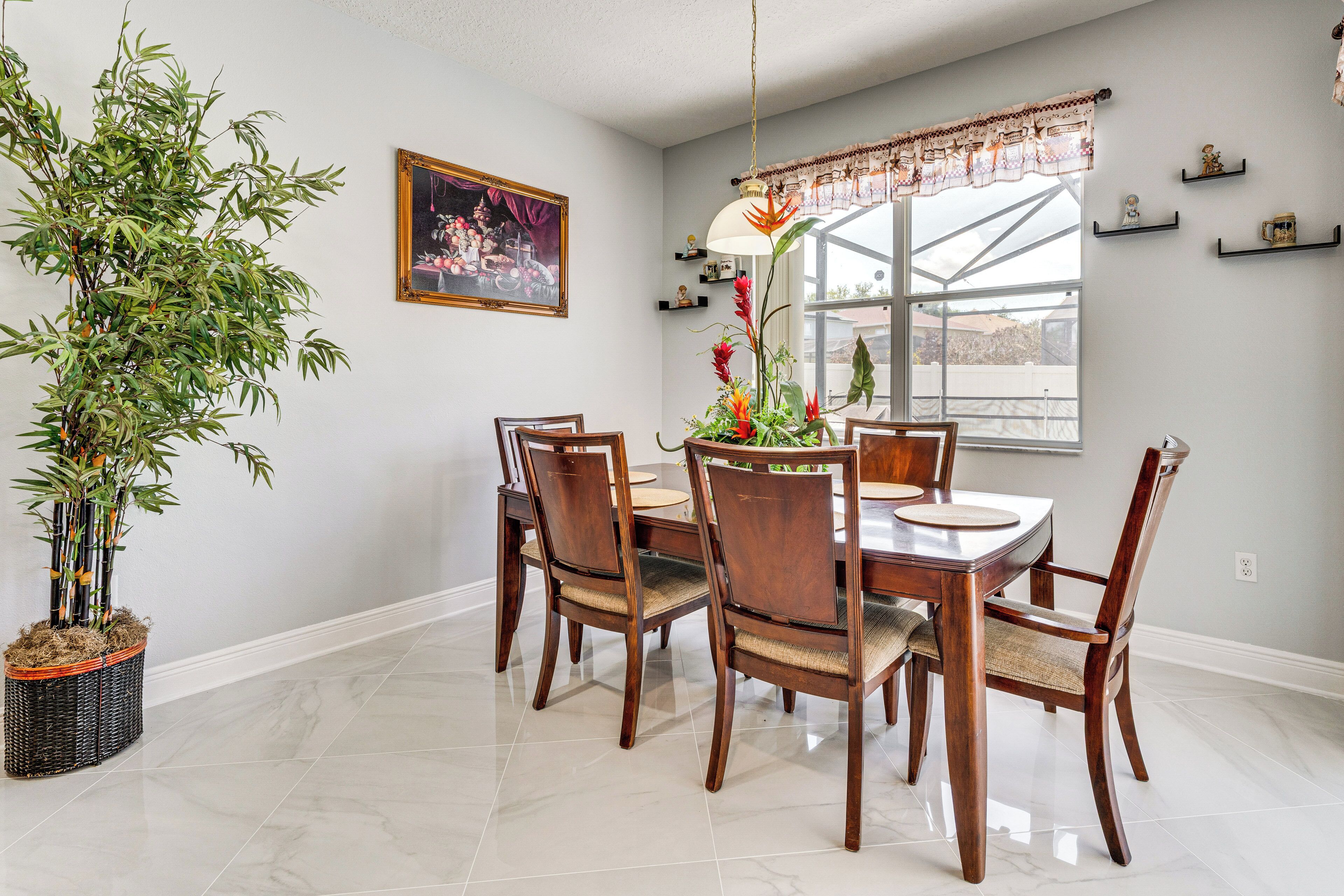 Un área de comedor con una mesa y sillas, una planta en maceta, una ventana con vistas y una lámpara colgante.