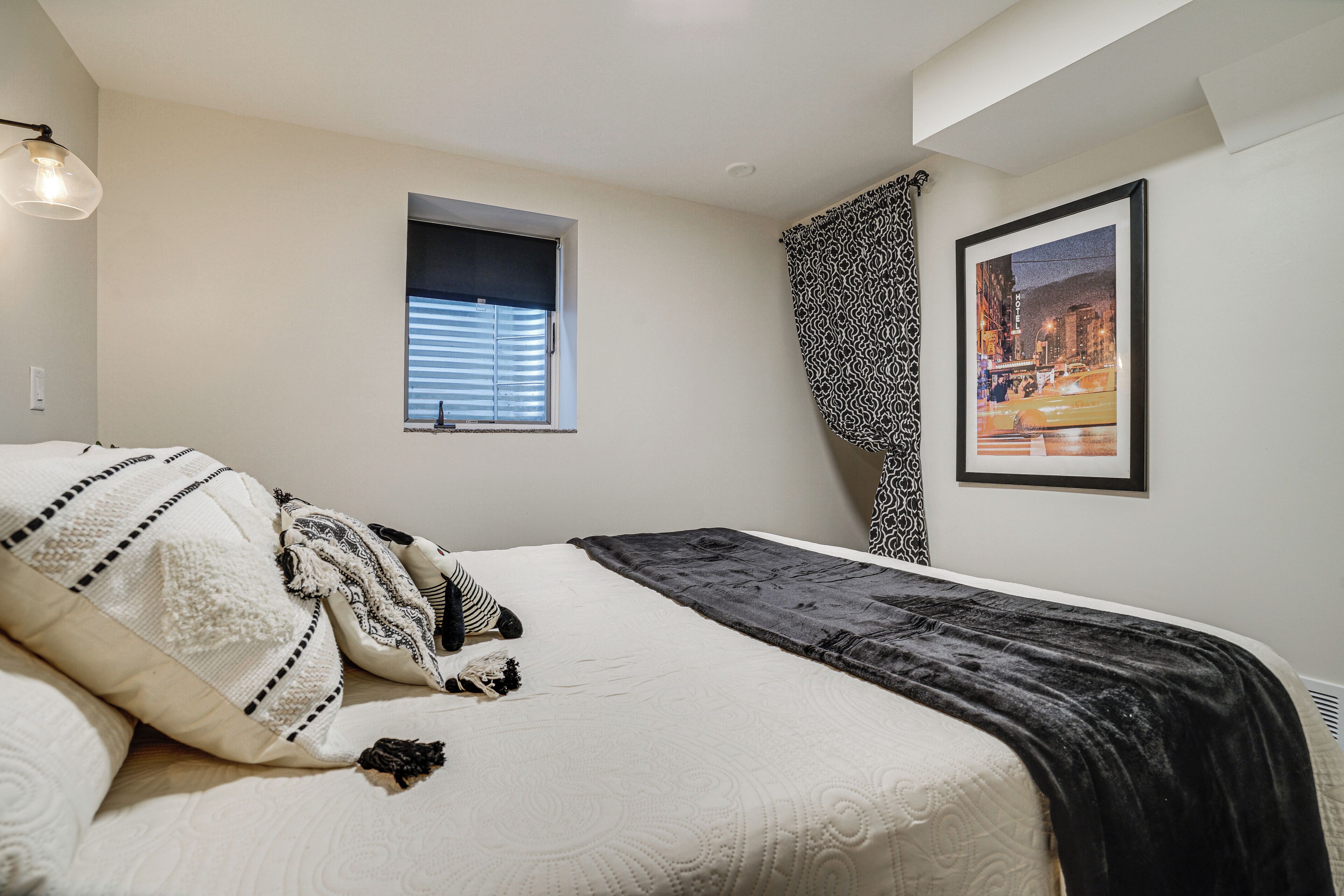 A bedroom with a bed, a window, a framed picture, and a patterned curtain.