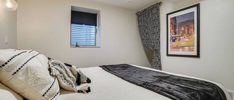 A bedroom with a bed, a window, a framed picture, and a patterned curtain.