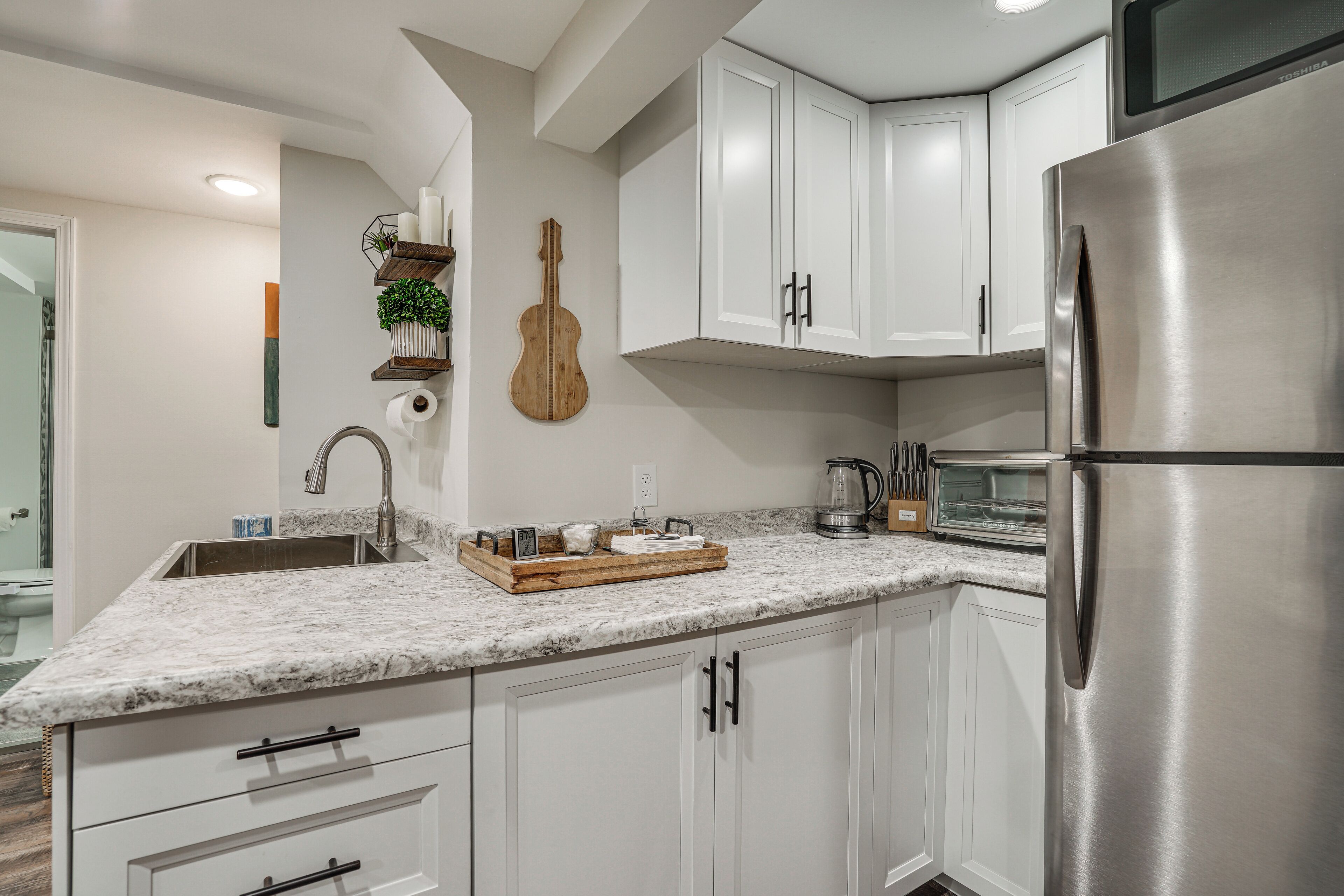 Una cocina moderna con armarios blancos, un refrigerador de acero inoxidable y una encimera de mármol.