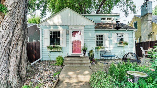 A quaint cottage with a red door, a small porch, and a garden with a birdbath. - Chic Minneapolis Apt - 6 Blocks to Lake Nokomis! (Minneapolis)